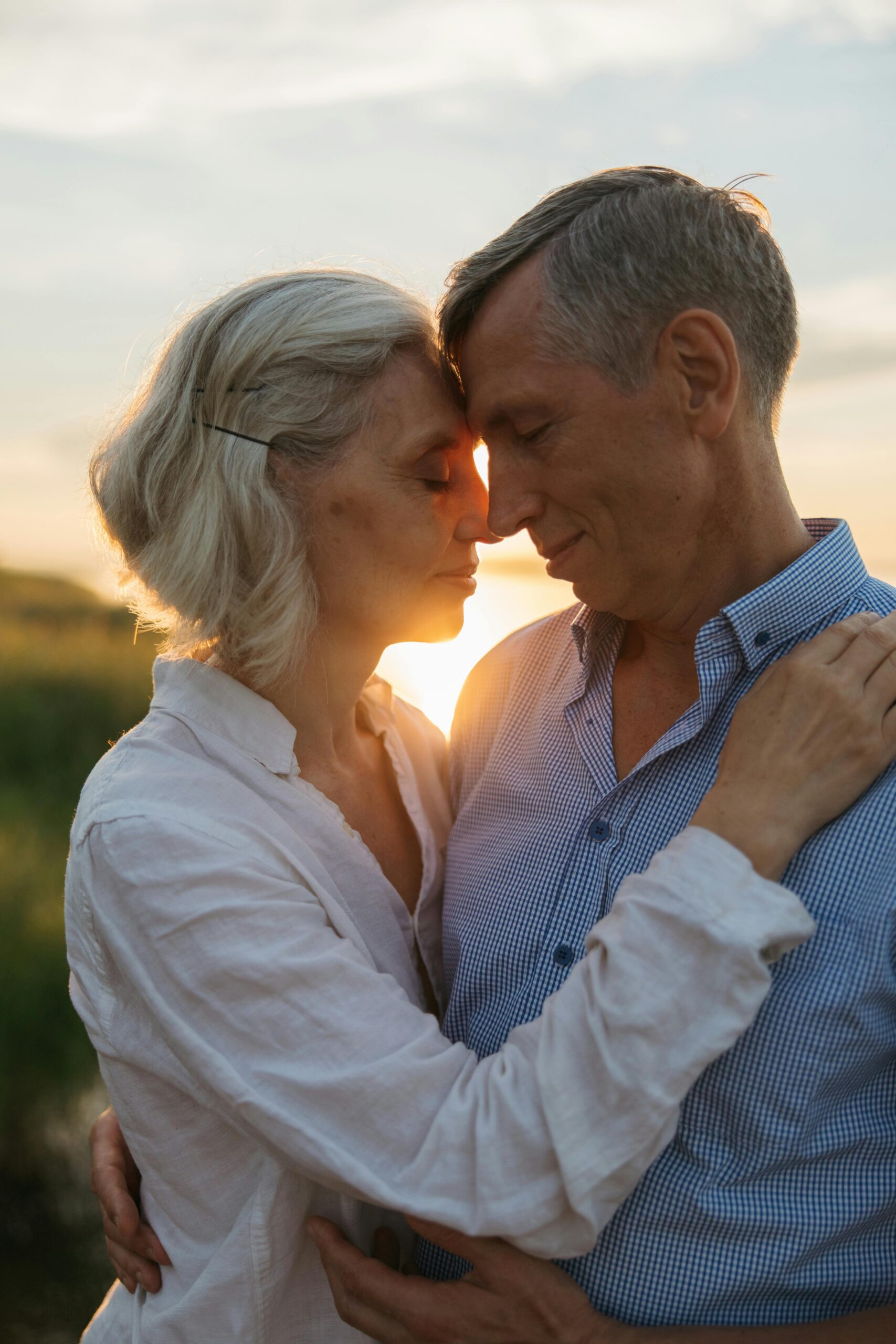 A senior couple lovingly embracing in a serene outdoor setting during sunset.